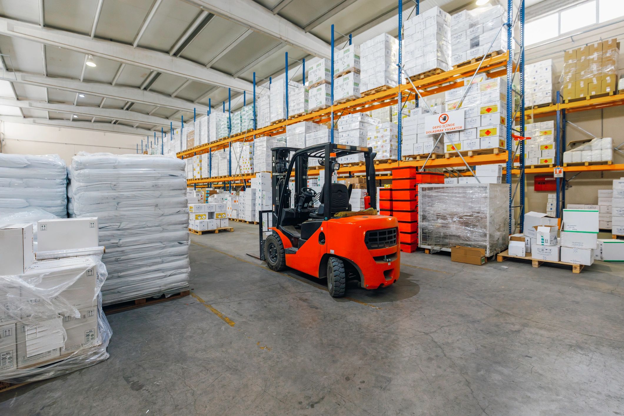 Forklift in warehouse aisle with stacked goods prepared for distribution